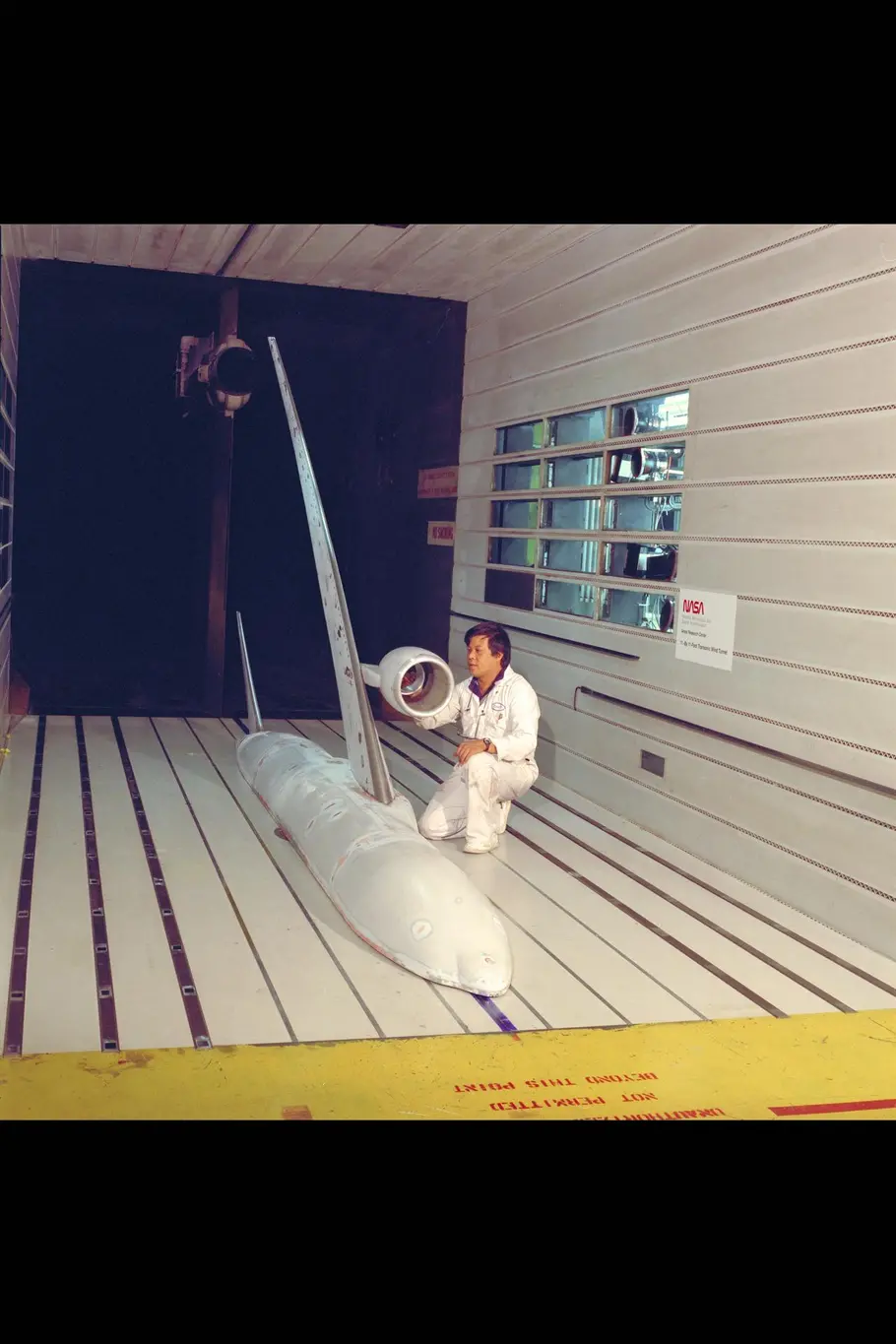 A photo of a man in a wind tunnel with a model of an airplane.
