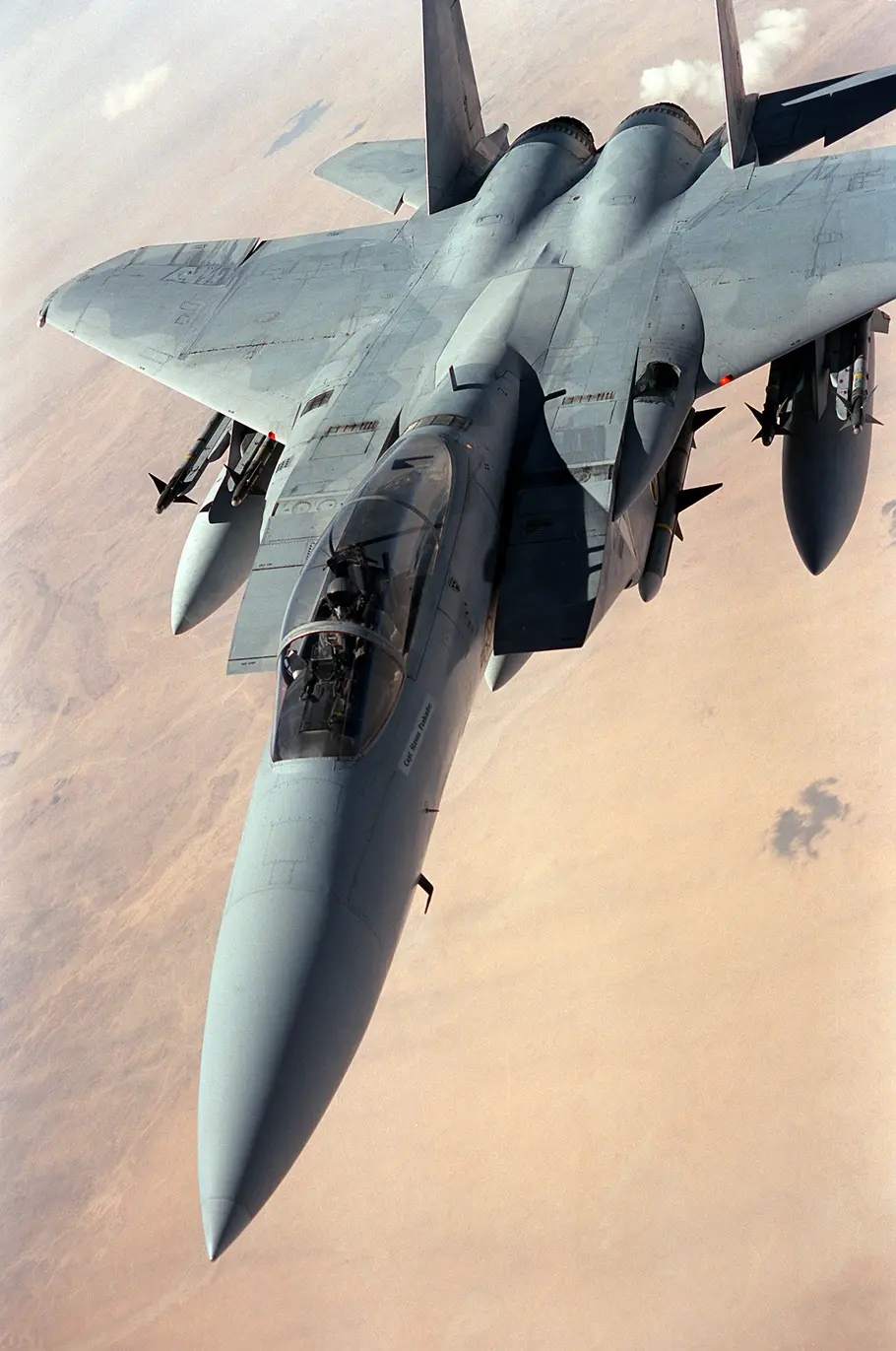 An F-15 fighter jet flying through the sky desert landscape in the background.