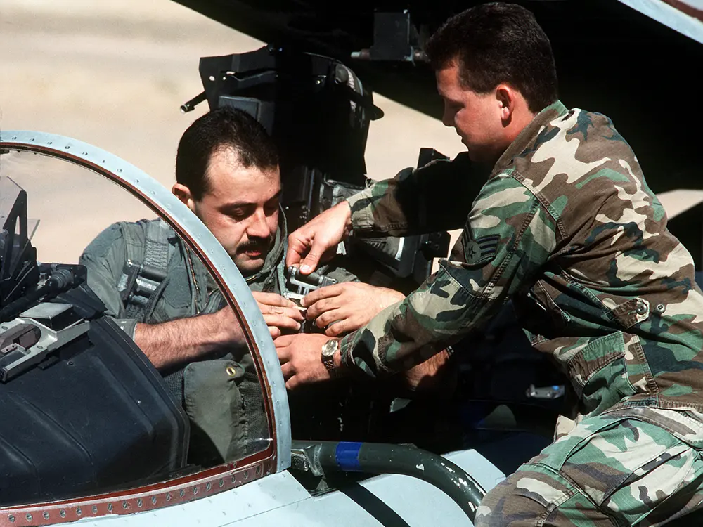 Two military personnel are interacting near the cockpit of a jet, with one seated inside and the other standing beside it, assisting with equipment adjustments. The jet displays the name "Capt. Rico Rodriguez."
