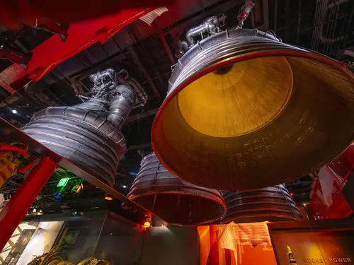 A large metal dome-like structure, as seen from underneath it, hangs from the ceiling. A mirror is used to create the illusion that there are four of these structures hanging.