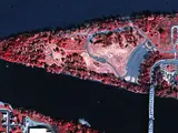 A near infrared aerial photo of a triangular shaped island that has a bridge connecting it to the mainland. The center of the island is a paler red.