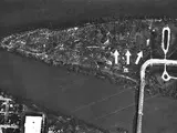 An aerial photo of a triangular shaped island that has a bridge connecting it to the mainland. Arrows point to dark spots at the center of the island.
