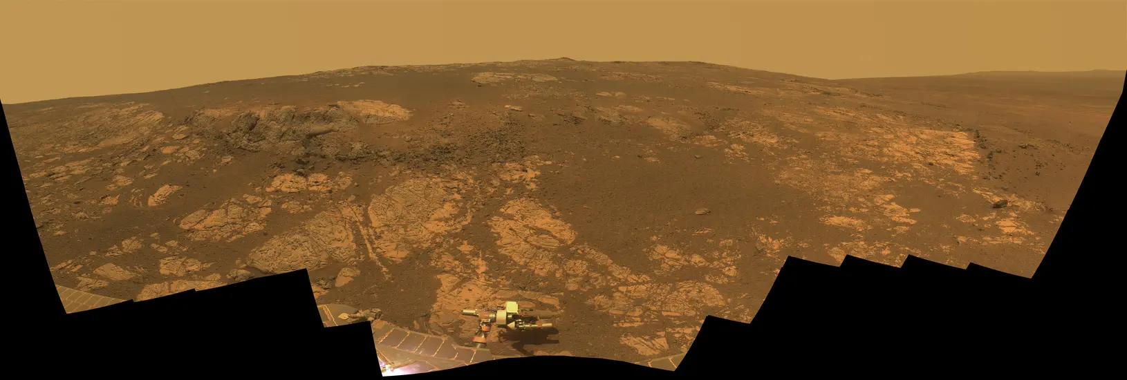 A panoramic view looking out over a hill of the dusty red terrain on Mars.