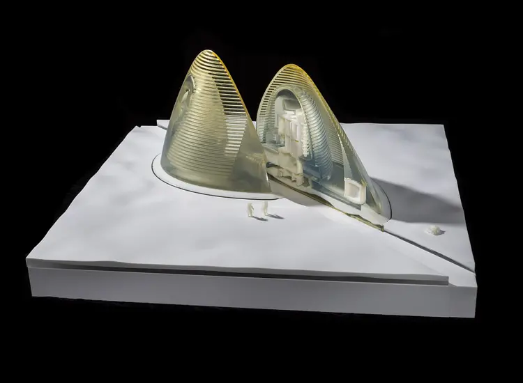 Model consists of a semi-translucent oval structure that has been split in half. This structure sits on a wavy white surface with two attached astronaut figurines and an unattached car/rover figuine. Model is lit by lights set below the two structures. Surface sits on a raised base with a solid base piece underneath this assembly. The model is uplit with low voltage LED strip lights. The habitat model is split in half to show the interior section and is composed of two 3d-printed translucent resin shells. The model sits on a milled white corian base.