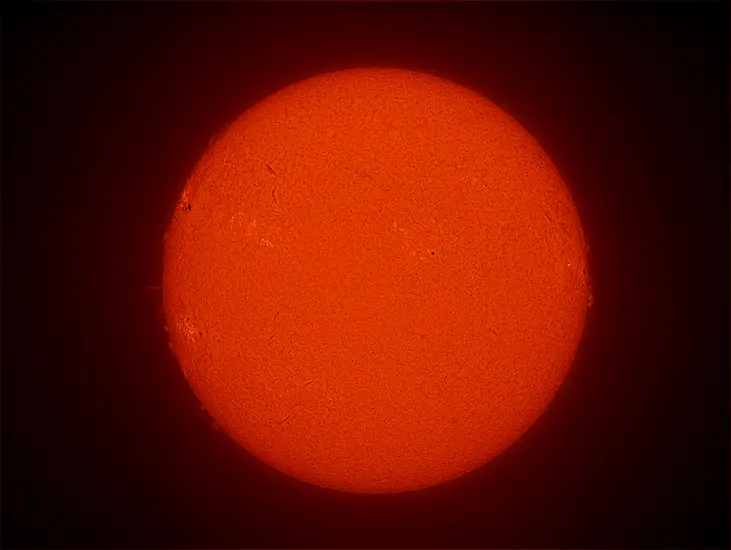 Disk view of the Sun with a large sunspot cluster visible on the left side of the Sun. 