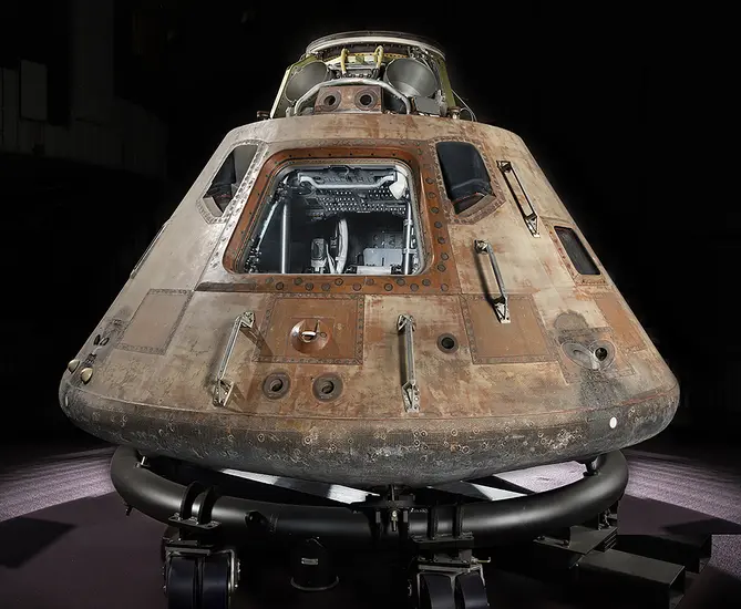 Picture of Apollo 11 Command module Columbia on a transportation rig. Module is lit from above and hatch is facing the camera.